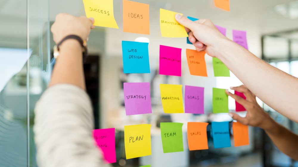 Business people arranging various adhesive notes with text on glass in office